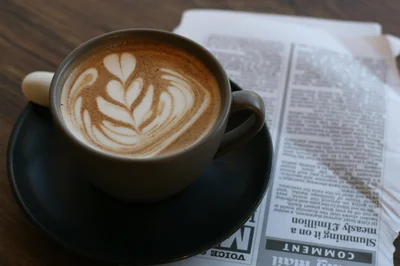A cup of latte art placed on a newspaper, perfect for a cozy coffee break.