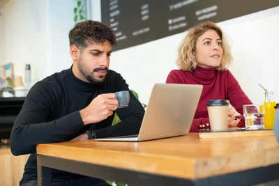 Professional discussion in a café with coffee and a laptop, showcasing teamwork and creativity.