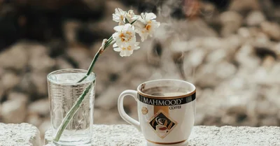 A steaming cup of coffee with a blooming white flower in a tranquil setting, perfect for a serene break.